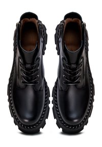 Black leather ankle boots featuring a thick, textured sole, front lacing, and side zippers for easy wear. Smooth finish with braided accents.