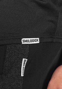 Pantalones cortos deportivos negros que presentan dos etiquetas de la marca SMILODOX, una en la cintura y otra en el costado, con un panel texturizado a lo largo de la pierna.