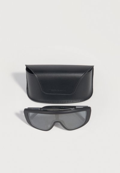 Μαύρα ορθογώνια γυαλιά ηλίου με σκούρους φακούς τοποθετημένα κάτω από μια καμπυλωτή μαύρη δερμάτινη θήκη σε λευκό φόντο.