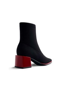 Stivaletti neri realizzati in tessuto testurizzato, con un'unica tomaia geometrica rossa e una punta a forma appuntita con un bordo a contrasto rosso.