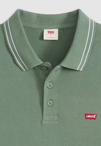 Green polo shirt with white stripes on collar, three buttons, and a small red Levi's logo on the left side. Textured fabric. Standard fit.