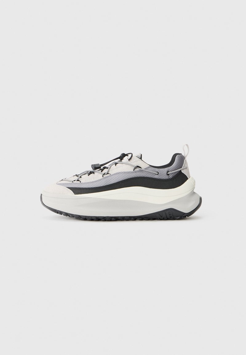 Zapatillas con un diseño estratificado en gris claro, negro y blanco. Cuentan con una parte superior texturizada, cordones elásticos y una suela gruesa y texturizada.
