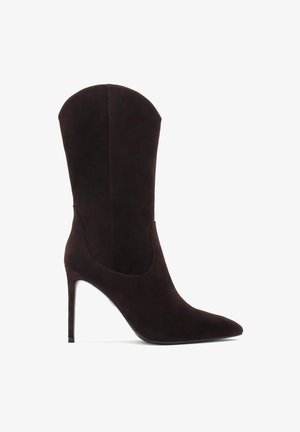 Brūnas zamšādas potītes zābaki ar norādītu purngalu, augstu stiletto papēdi un unikālu izliekta izgriezuma dizainu uz zābaka kājas, kas nodrošina elegantu siluetu.