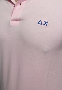 Polo shirt rosa chiaro in tessuto texture, con logo ricamato blu composto da forme geometriche nella zona del petto.