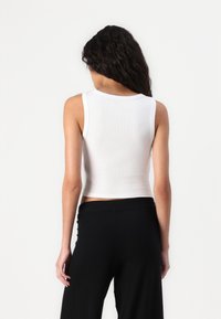 White cropped tank top in ribbed fabric with a round neckline and wide armholes, paired with black wide-leg pants.