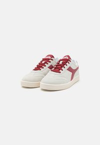 Hvite og røde semskede sneakers med teksturert overflate, med røde lisser og en kontrastfarget side stripe. Gummisåle for godt grep.