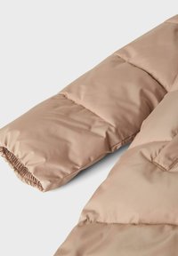 Vadderad jackärm i mjuk beige färg. Har en slät, blank yta, elastiska manchetter och ett kviltat mönster för isolering.