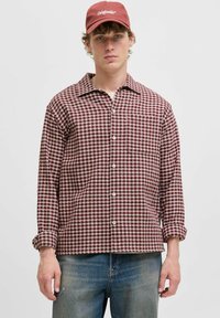 Rød og hvid ternet flannel skjorte med fold-down krave og forreste knapper, parret med blå denim jeans og en maroon baseball cap.