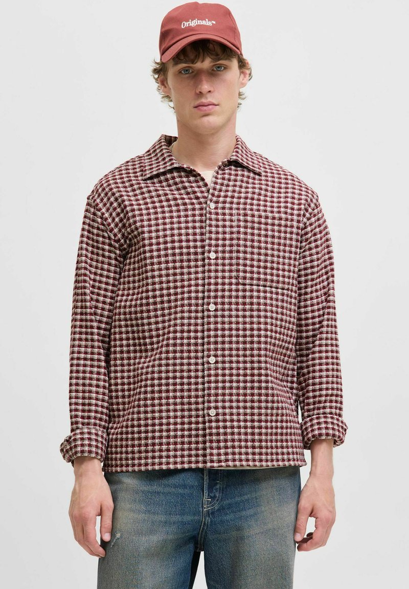 Rød og hvid ternet flannel skjorte med fold-down krave og forreste knapper, parret med blå denim jeans og en maroon baseball cap.
