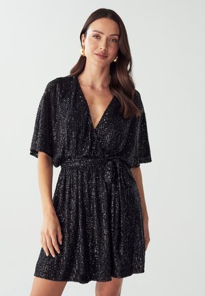 Black sequin dress with a deep V-neck and short sleeves. Features a tie waist and pleated skirt. Reflective sequins create a shimmering effect.