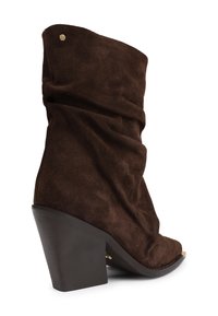 Botine din suede maro, cu un design lejer, vârf ascuțit și toc gros negru. Accente de hardware notabile în partea de sus.