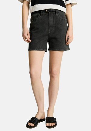 Persoon draagt zwarte denim shorts met een zwarte riem, een zwart-wit gestreept topje en zwarte open teenslippers.