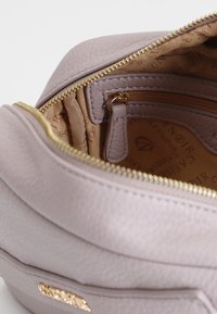 Lyse lilla lædertaske indeni med gylden lynlås, der har et mønstret foder og en lynlås lomme, der fremhæver en glat tekstur og en struktureret form.