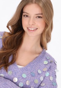 Fioletowy wełniany sweter z dekoltem w kształcie litery V, ozdobiony błyszczącymi, okrągłymi, iryzującymi cekinami na przodzie. Miękka tekstura, luźny krój.