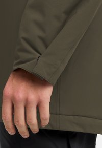 Olijfgroene jacksleeve, gemaakt van glad, waterafstotend materiaal. Heeft een fitted manchette met een klein knoopdetail nabij de pols.