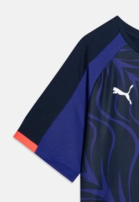 Majica s kratkimi rokavi iz temno modrega blaga s purpurnimi valovitimi vzorci. Ima zračen mrežast del in koralni naglas na rokavu.