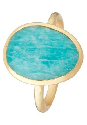 Bague en or avec une pierre turquoise ovale irrégulière sertie dans un simple chaton, montrant la texture naturelle de la pierre et ses variations de couleur.