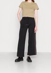 Randig beige och mörkbrun t-shirt, kombinerad med svarta vida byxor med sidostråkar. Svarta kraftiga skor fulländar outfiten.