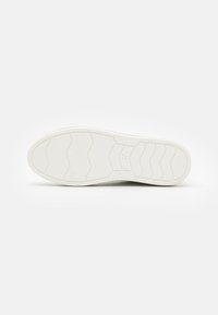 Biała podeszwa sneakersów z teksturowaną gumową podeszwą z falistym wzorem przyczepności i wskaźnikiem rozmiaru "37" wytłoczonym w pobliżu pięty.