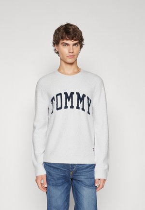 Maglione grigio chiaro realizzato in tessuto fluffy, con grande scritta in blu navy "TOMMY" sulla parte anteriore. Abbinato a jeans blu.