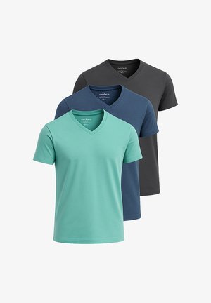 Mand iført mørkegrå V-hals T-shirt og blå jeans, kigger til venstre med sort ur på venstre håndled mod hvid baggrund.