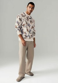 Knit sweater in cream with multicolored abstract patterns, paired with beige straight-leg pants and gray slip-on shoes.