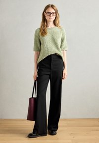 Textured, light green sweater with short sleeves, paired with high-waisted black wide-leg trousers. Black shoes and a burgundy tote bag.