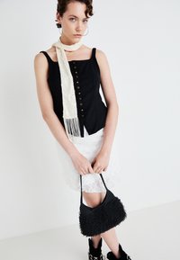 Svart korsett-topp med knapper, hvit blondekjole, beige frynset skjerf, teksturert svart håndveske og svarte snøring støvler. Enkelt, men definert design.