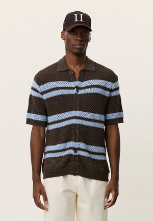 Brun og lyseblå stribet kortærmet striktrøje med knappelukning foran og krave; båret med en sort baseballkasket.