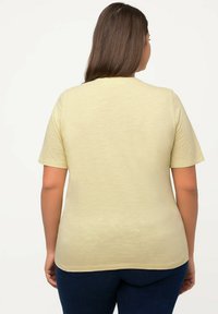 Maglietta gialla chiaro a maniche corte con una texture liscia, vestibilità rilassata e scollatura rotonda, abbinata a jeans blu scuro.