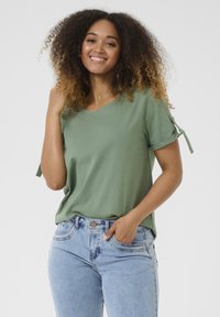 Green short-sleeve T-shirt with a V-neck and tied accents on sleeves. Worn with high-waisted blue denim jeans and a casual pose.