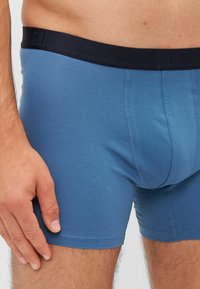 Kék pamut boxer nadrág sötét derékpánttal, amelyen a "GAP" logó látható. A dizájn testhez simuló, sima, rugalmas anyagból készült, lapos varrásokkal.