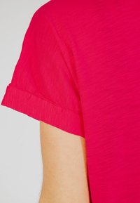 Top corto fucsia a maniche corte con un delicato pattern testurizzato. Il bordo delle maniche presenta una finitura semplice e pulita. Il materiale sembra leggero e morbido.