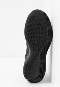 Suela de zapato deportivo negro con goma texturizada, que presenta un patrón de crestas y protuberancias para un mejor agarre, forma curva y bordes suaves.