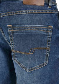 Blauwe spijkerbroek met een achterzak met hoekige stiksels en een bruin leren label op de tailleband.