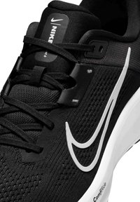 Sort Nike sneakers med en struktureret syntetisk overdel, hvid swoosh-logo, flade snørebånd og en polstret hvid mellemsål.