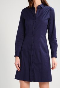 Marinblå knapp-up klänning i slätt tyg, med långa ärmar, krage och figursydd midja som går till mitten av låret.