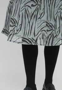 Sort og hvid stribet knælang kjole med struktureret stof, parret med sorte leggings og flade, sorte sko.