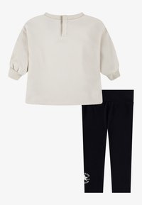 Maglione a maniche lunghe color beige chiaro con colletto e polsini a coste, abbinato a leggings neri con un accento di logo circolare sull'orlo.