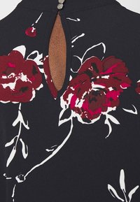 Tissu noir à motif floral bordeaux et blanc. Présente une ouverture en forme de goutte d'eau à l'arrière, agrémentée d'un bouton rond en argent.