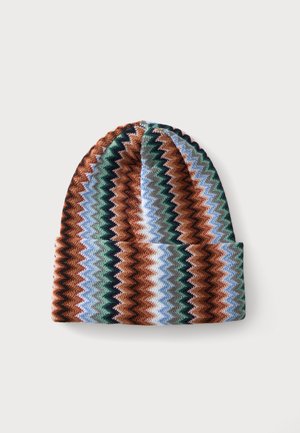 Bonnet tricoté avec des rayures en motif zigzag en marron, vert, bleu, blanc et noir, replié sur le bord inférieur sur un fond uni.