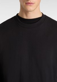 Schwarzer Rundhals-Pullover aus Baumwolle, mit einer glatten Textur und genähtem Halsauschnitt. Er hat eine lockere Passform und ein minimalistisches Design.