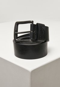 Schwarzer Leder-Gürtel mit einer rechteckigen metallischen Schnalle und prägierter Markenbezeichnung. Der Riemen ist glatt und die Schnalle hat eine matte Oberfläche.