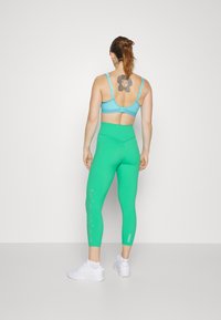Jasnoniebieski stanik sportowy z regulowanymi ramiączkami; zielone legginsy typu high-waisted z białym napisem "traction" po boku; białe sneakersy.