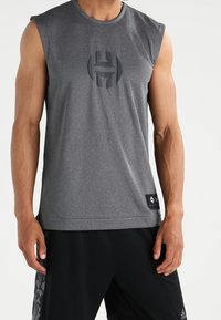 Débardeur de sport gris avec un col rond. Présente un logo en relief sur la poitrine et une étiquette sur l'ourlet inférieur. Confectionné en tissu lisse et extensible.