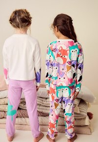 Två barn har på sig pyjamas. Den ena har en vit överdel och lila byxor med färgpluttar. Den andra har ett mönster med flerfärgade djur.