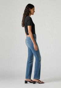 Czarny t-shirt z krótkim rękawem w połączeniu z jasnoniebieskimi dżinsami w kształcie dzwonów, posiadającymi tylne kieszenie i brązową skórzaną metkę przy pasku. Czarne sandały na obcasie.