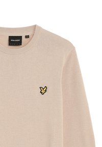 Beige sweater with ribbed round neckline. Features a black and yellow embroidered logo on the left chest. Soft texture with long sleeves.