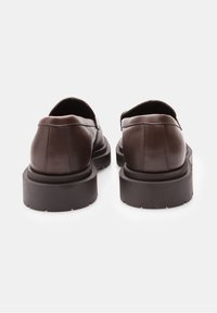 Chaussures en cuir marron avec une texture lisse, une forme arrondie et une semelle épaisse en caoutchouc noir. Présentent une couture minimale et un détail avec une languette arrière.