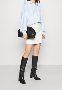 Lys blå hoodie med et marmor mønster, hvide snore, hvid denim mini skirt, sorte læder knæhøje støvler og en sort clutch-task.